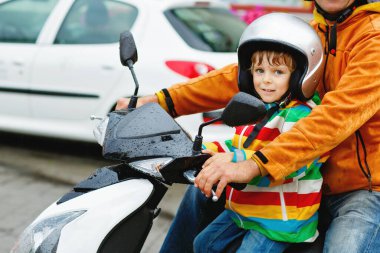 Kasklı küçük bir çocuk ve şehirde motosikletle gezen babası. Mutlu çocuk babasıyla birlikte motosiklet yolcusu. Güvenli ve güvenli bir şekilde araçlarda çocuklar var. Erkek çocuğu tutar..