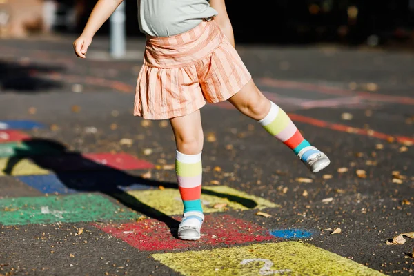 Close-up de pernas de menina pequena criança jogando hopscotch jogo desenhado com giz coloridos no asfalto. Pequena criança ativa pulando no playground ao ar livre em um dia ensolarado. Atividades de verão para crianças. — Fotografia de Stock