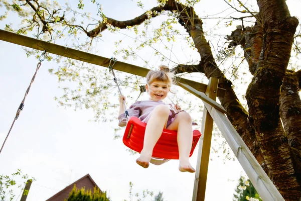 Menina pequena feliz que se diverte no balanço no jardim doméstico. Sorrindo positivo criança saudável balançando no dia ensolarado. Menina pré-escolar rindo e chorando. Lazer ativo e atividade ao ar livre. — Fotografia de Stock