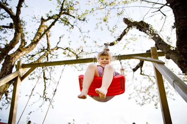 Menina pequena feliz que se diverte no balanço no jardim doméstico. Sorrindo positivo criança saudável balançando no dia ensolarado. Menina pré-escolar rindo e chorando. Lazer ativo e atividade ao ar livre. — Fotografia de Stock