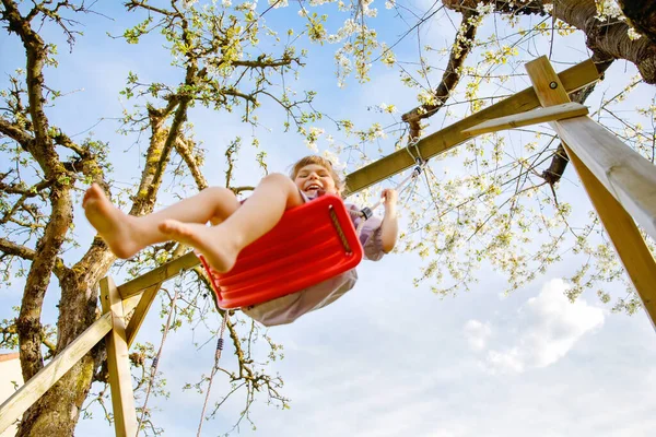 Menina pequena feliz que se diverte no balanço no jardim doméstico. Sorrindo positivo criança saudável balançando no dia ensolarado. Menina pré-escolar rindo e chorando. Lazer ativo e atividade ao ar livre. — Fotografia de Stock