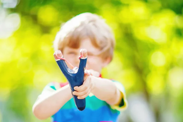 Rolig liten pojke skjuta trä slangbella mot gröna träd bakgrund. Barnet har roligt på sommaren — Stockfoto