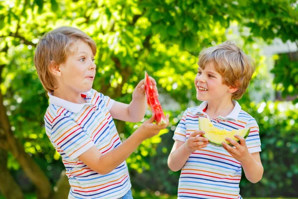 Dois meninos pré-escolares com cabelos loiros comendo melancia vermelha e amarela no jardim de verão. Crianças felizes engraçadas sorrindo e degustando lanche de frutas saudáveis no dia ensolarado. Irmãos, gêmeos e melhores — Fotografia de Stock