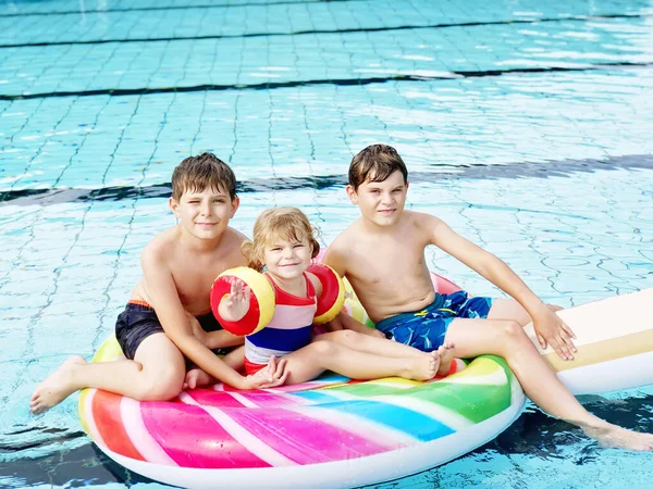 Tres niños, dos niños y una niña chapotean en una piscina al aire libre en verano. Niños felices, hermanos y hermanas jugando en una enorme piruleta inflable de chicle disfrutando de un clima soleado en la piscina pública. —  Fotos de Stock