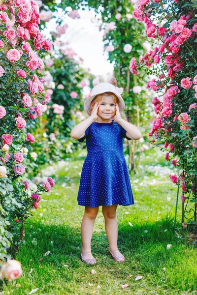 Portret van een kleuter in een bloeiende rozentuin. Schattig mooi mooi kind dat plezier heeft met rozen en bloemen in een park op zomerse zonnige dag. Gelukkig lachende baby. — Stockfoto