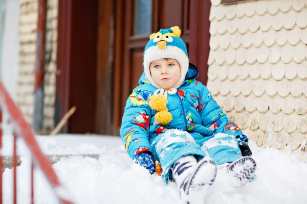 Netter kleiner Vorschuljunge in bunter Winterkleidung, der bei Schneefall im Freien mit Schnee und Schneeflocken spielt. Aktive Freizeitgestaltung im Freien mit Kindern im Winter. Glückliches Kind rutscht auf Heimtreppe — Stockfoto