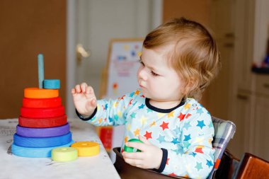 Evde ya da çocuk odasında eğitici oyuncaklarla oynayan sevimli, küçük bir kız bebek. Mutlu sağlıklı çocuk renkli tahta gökkuşağı oyuncak piramidiyle eğleniyor. Çocuk farklı yetenekler öğreniyor.