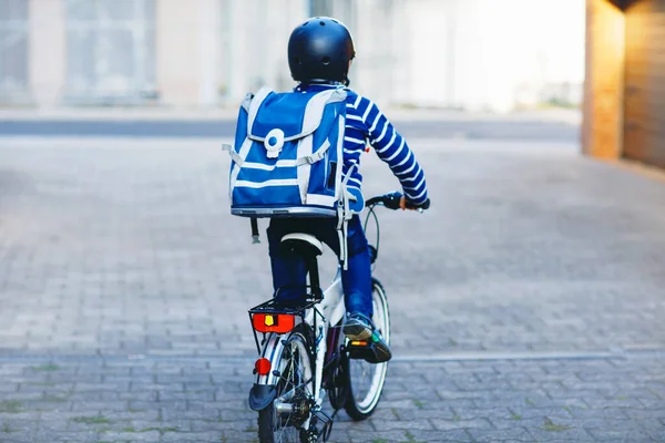 Iskolás fiú, bukósisakban biciklivel a városban, hátizsákkal. Boldog gyermek színes ruhában biciklizés kerékpárral úton az iskolába. Biztonságos út a gyerekeknek az iskolába. — Stock Fotó