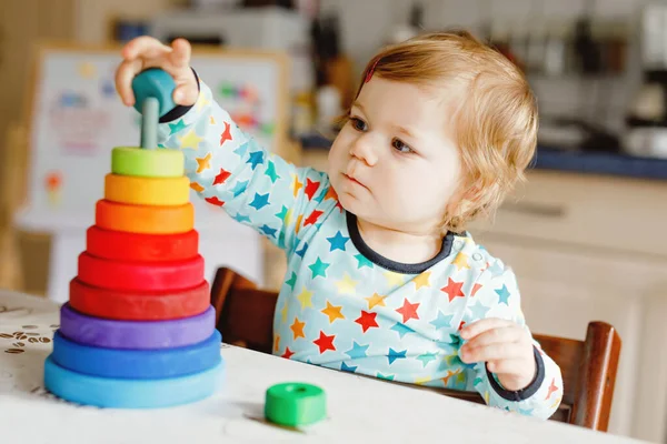 Söt vacker liten flicka leker med pedagogiska leksaker hemma eller på dagis, inomhus. Glad frisk barn har kul med färgglada trä regnbåge leksak pyramid. Grabben lär sig olika färdigheter. — Stockfoto