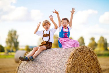 Buğday tarlasında geleneksel Bavyera kostümlü iki çocuk. Alman çocukları Ekim Festivali sırasında saman balyasında oturuyorlar. Almanya 'da yaz aylarında erkek ve kız saman balyalarında oynarlar. En iyi arkadaşlar.