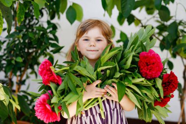 Kocaman bir buket kırmızı ve pembe şakayık çiçekleri olan sevimli küçük kız. Sıcak bir bahar ya da yaz günü, aile bahçesinde gülümseyen anaokulu çocuğunun portresi. Yaz zamanı..