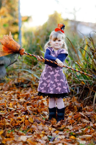 可爱的小女孩穿着巫婆的衣服庆祝万圣节。快乐的孩子在户外,戴着橙色滑稽的帽子,拿着巫婆的扫帚.10月是一个美丽的家庭节日。户外活动 — 图库照片
