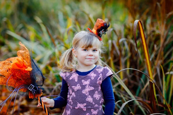 El retrato de una niña pequeña vestida de bruja celebra Halloween. Niño feliz al aire libre, con sombrero naranja divertido y escoba de bruja. Hermosa temporada de festivales familiares en octubre. Actividades al aire libre —  Fotos de Stock