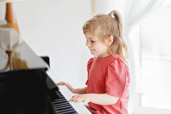 Beautiful little toddler girl playing piano in living room. Cute preschool child having fun with learning to play music instrument. Early musical education for children. — Stock Photo, Image