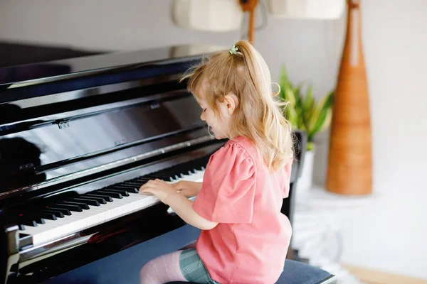 Smuk lille pige, der spiller klaver i stuen. Sød førskolebarn har det sjovt med at lære at spille musikinstrument. Tidlig musikalsk uddannelse for børn. - Stock-foto