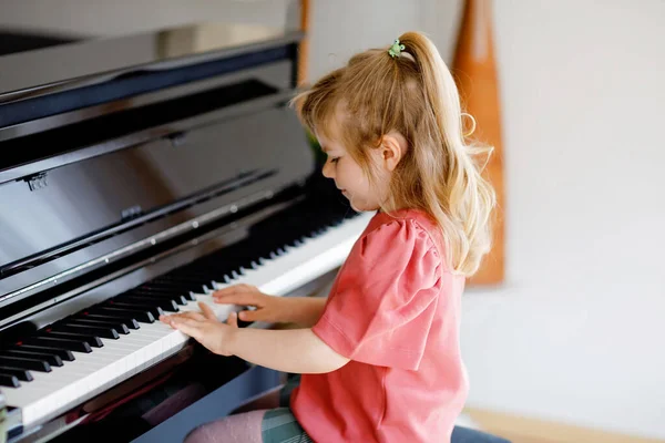 Smuk lille pige, der spiller klaver i stuen. Sød førskolebarn har det sjovt med at lære at spille musikinstrument. Tidlig musikalsk uddannelse for børn. - Stock-foto