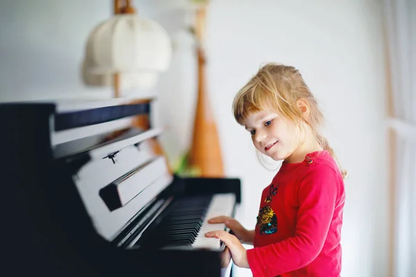 Mooi klein peutermeisje dat piano speelt in de woonkamer. Schattig kleuter die plezier heeft met het leren spelen van muziekinstrumenten. Voorschools muziekonderwijs voor kinderen. — Stockfoto