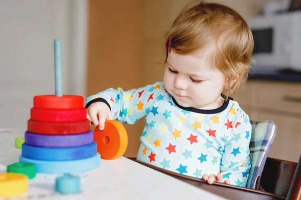 Bonito linda menina brincando com brinquedos educativos em casa ou berçário, dentro de casa. Criança saudável feliz se divertindo com pirâmide de brinquedo colorido arco-íris de madeira. Aprendizagem de crianças habilidades diferentes. — Fotografia de Stock