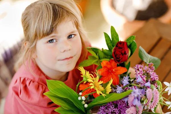 Kleines Vorschulmädchen mit Blumenstrauß zu Hause. Kleinkind legt bunte Gartensommerblumen in kleine Fläschchen mit Wasser. Aktivitäten für Kinder zu Hause. Blumen in Regenbogenfarben. Glückliches Kind. — Stockfoto