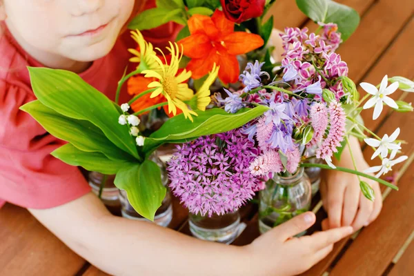 Close up of little preschool girl with flower bouquet at home. Close-up of toddler child and colorful garden summer flowers in small bottles with water. Closeup of flowers in rainbow colors. — Stock Photo, Image