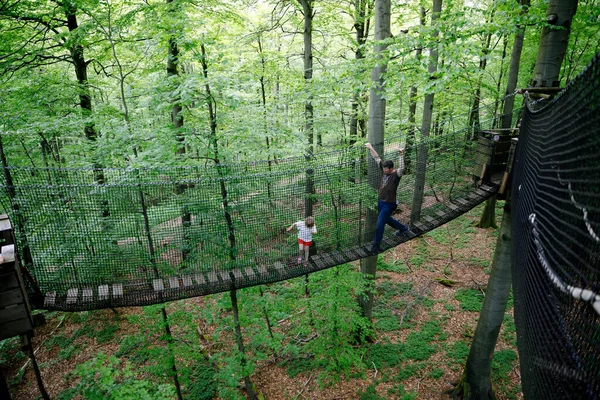 Kleine Vorschulmädchen und ihr Vater gehen auf einem hohen Baumwipfelpfad mit Holzsteg und Seilbahnen. Glückliches aktives Kind und Vater, junger Mann erkundet Baumwipfelpfad. Lustige Aktivitäten für Familien im Freien — Stockfoto