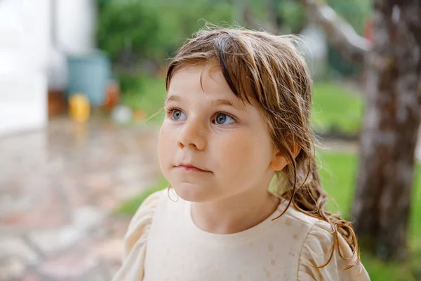 Pequena menina pré-escolar correndo através de chuva de verão pesado no jardim. Feliz sorrindo criança criança molhada se divertindo com espirrar e jumpin em poças. Atividade para crianças no dia do tempo chuvoso. — Fotografia de Stock