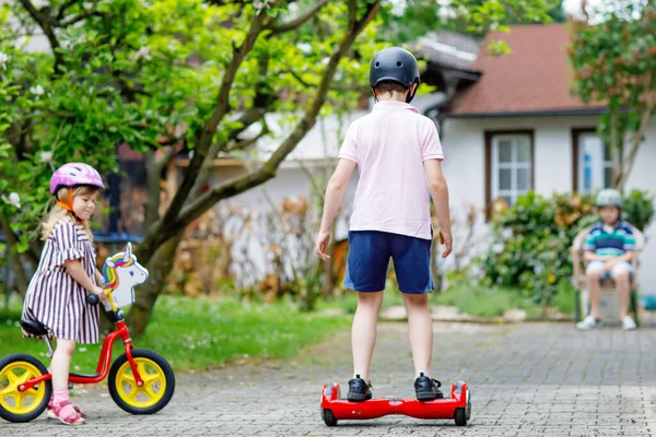 Menina da criança correndo com bicicleta de equilíbrio. Rapaz da escola a bordo. Duas crianças felizes se divertindo com gadgets modernos, atividade ao ar livre. Felicidade, infância. Excercise para crianças. — Fotografia de Stock