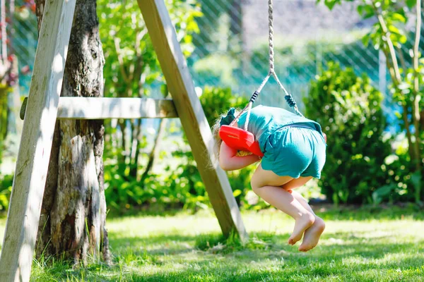 Happy little preschool girl having fun on swing in domestic garden. Healthy toddler child swinging on sunny summer day. Children activity outdoor, active smiling kid laughing — Stock Photo, Image