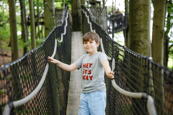 Niño preadolescente caminando por el sendero alto del dosel del árbol con pasarela de madera y cuerdas en Hoherodskopf en Alemania. Feliz niño pequeño y activo explorando el sendero de la copa de un árbol. Actividad divertida para familias al aire libre — Foto de Stock