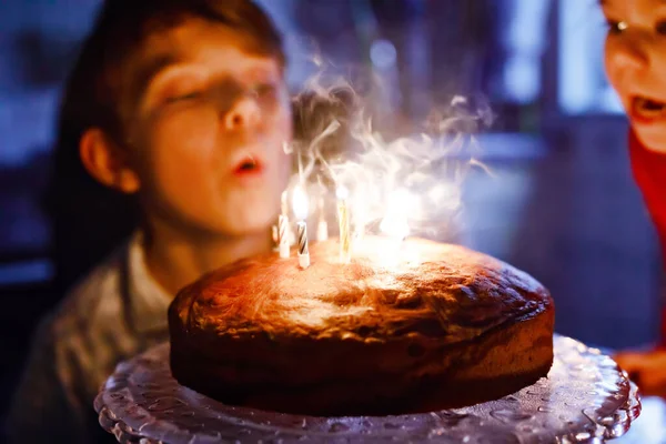 Imádnivaló szőke kisfiú, aki a születésnapját ünnepli. Gyertyákat fúj házi süteményre, beltérben. Születésnapi party iskolásoknak, családi ünnep — Stock Fotó