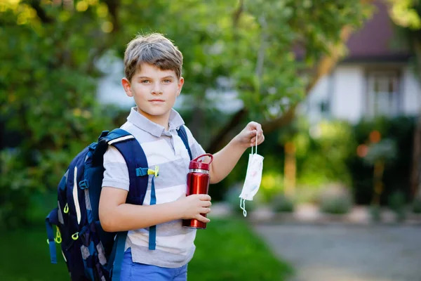 Küçük mutlu çocuk, tıbbi maske, su şişesi, sırt çantası ya da sırt çantası. Okul çocuğu okula gidiyormuş. Sağlıklı bir çocuk. Corona salgınından sonra karantina sonrası okula dönüş. — Stok fotoğraf