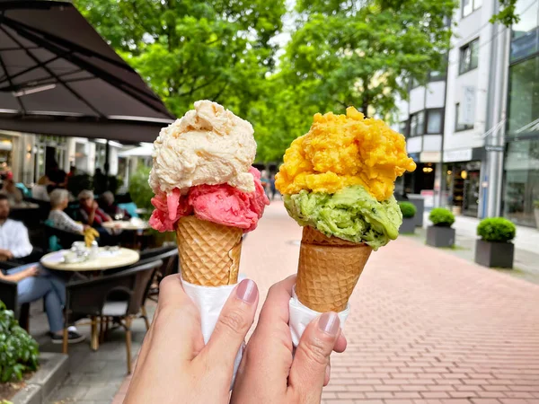 Jeune femme mains tenant des cônes de crème glacée le jour de l'été dans la ville. Savoureux fruits colorés et crème glacée aux baies — Photo