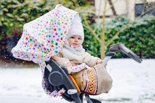 Schattig klein mooi baby meisje zittend in de kinderwagen of kinderwagen op koude besneeuwde winterdag. Gelukkig lachend kind in warme kleren, mode stijlvolle babyjas. Babys eerste sneeuw. Winterwandeling buiten. — Stockfoto