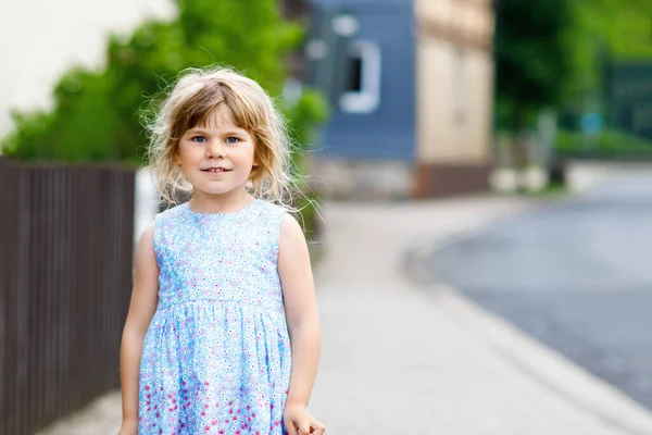 Porträtt av glada leende småbarn flicka utomhus. Ett litet barn med blont hår som tittar och ler mot kameran. Glad frisk barn njuta av utomhus aktivitet och spela. — Stockfoto