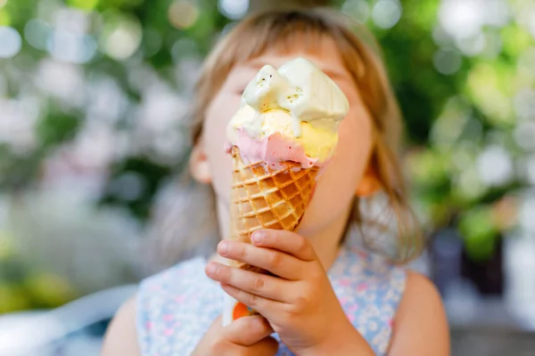 Маленькая дошкольница ест мороженое в вафельном рожке в солнечный летний день. Счастливый малыш ест десерт из мороженого. Сладкая еда в жаркие летние дни. Яркий свет, красочное мороженое — стоковое фото