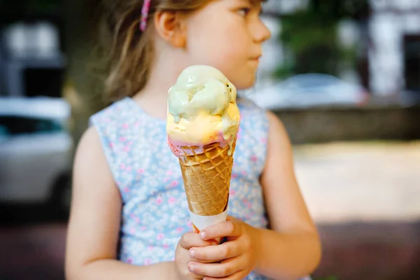 Petite fille d'âge préscolaire mangeant de la crème glacée dans un cône de gaufre le jour ensoleillé d'été. Happy enfant en bas âge manger dessert glacé. Nourriture sucrée pendant les chaudes journées d'été. Lumière vive, crème glacée colorée — Photo