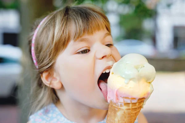Маленькая дошкольница ест мороженое в вафельном рожке в солнечный летний день. Счастливый малыш ест десерт из мороженого. Сладкая еда в жаркие летние дни. Яркий свет, красочное мороженое — стоковое фото
