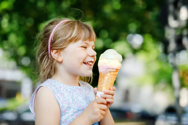Petite fille d'âge préscolaire mangeant de la crème glacée dans un cône de gaufre le jour ensoleillé d'été. Happy enfant en bas âge manger dessert glacé. Nourriture sucrée pendant les chaudes journées d'été. Lumière vive, crème glacée colorée — Photo