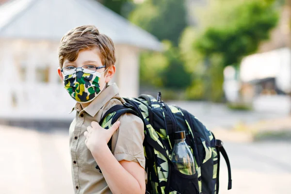 코로나 바이러스때문에 안경을 쓰고 의료용 마스크를 쓴 행복 한 소년. 화창 한 날 학교에 가는 길에 사첼을 데리고 버스를 기다리는 학생. 밖의 길거리의 건강 한 아이. — 스톡 사진