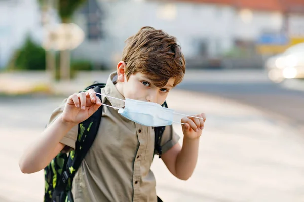 코로나 바이러스때문에 안경을 쓰고 의료용 마스크를 쓴 행복 한 소년. 화창 한 날 학교에 가는 길에 사첼을 데리고 버스를 기다리는 학생. 밖의 길거리의 건강 한 아이. — 스톡 사진