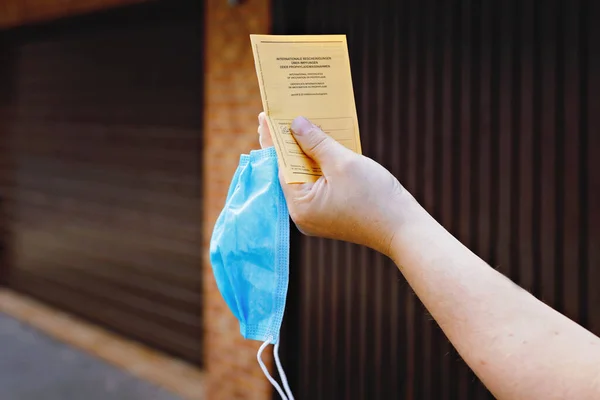 Closeup of man holding German inernational certificate of the vaccination and medical mask. Adult showing the information about vaccine against covid 19 corona virus. no face — Stock Photo, Image