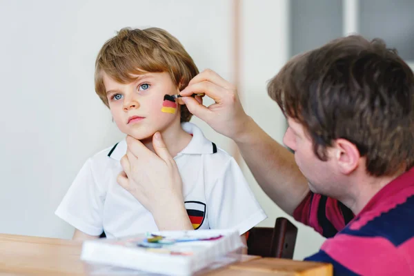 Giovane papà pittura bandiera sul viso del piccolo figlio per il calcio o gioco di calcio. — Foto Stock