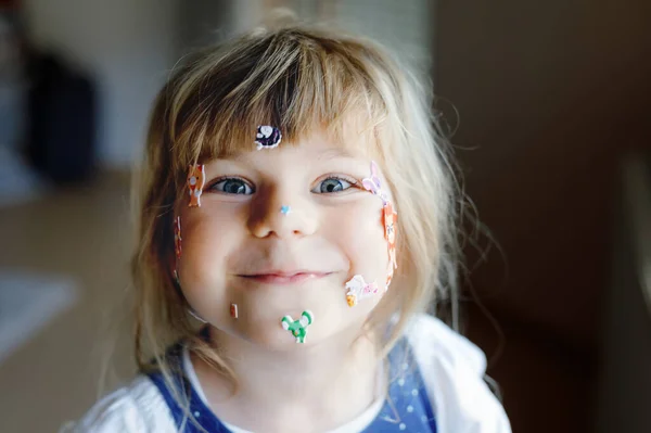 Kleines Mädchen spielt mit verschiedenen bunten Tieraufklebern. Konzept der Aktivität von Kindern während der Coronavirus-Quarantäne. Glückliches lustiges Kind, das Spaß mit Sticker im Gesicht hat. — Stockfoto