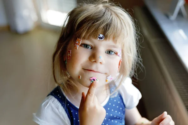 Pequeña niña jugando con diferentes pegatinas de animales de colores. Concepto de actividad de los niños durante la cuarentena del virus de la corona pandémica. Feliz niño divertido divertirse con pegatinas palo en la cara. — Foto de Stock