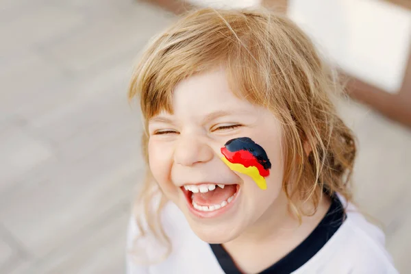 Niña rubia en edad preescolar viendo el partido de fútbol en público. Feliz alegre niño emocionado acerca de ganar el partido de partido de la selección de fútbol nacional favorita. chica con bandera alemana en la cara. —  Fotos de Stock