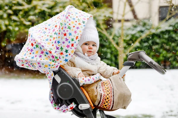 Bonito pequena menina bonita sentada no carrinho de bebê ou carrinho no dia frio de inverno nevado. Criança sorridente feliz em roupas quentes, moda casaco de bebê elegante. Bebês primeiro neve. Passeio de inverno ao ar livre. — Fotografia de Stock