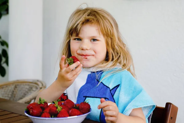 Malá školačka, co jí čerstvé jahody. Rozkošné dítě ochutnávka a kousání zralé jahody. Zdravé jídlo, dětství a vývoj. Šťastné dítě doma nebo v jeslích. — Stock fotografie