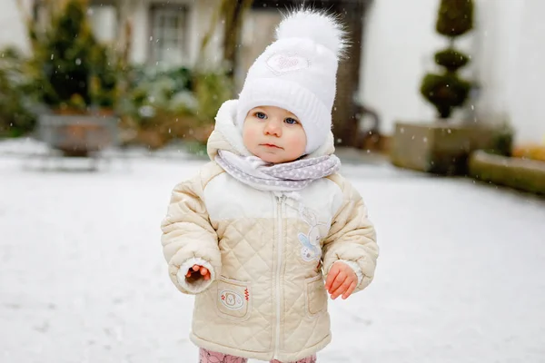 Bonne petite fille qui fait ses premiers pas à l'extérieur en hiver à travers la neige. Bébé mignon apprenant à marcher. Enfant qui s'amuse par temps froid et neigeux. Bébés première neige, activité. Promenade hivernale en plein air — Photo