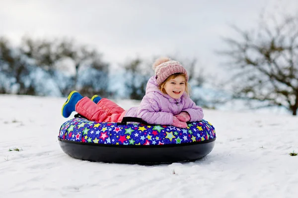 Active toddler girl sliding down the hill on snow tube. Cute little happy child having fun outdoors in winter on sledge . Healthy excited kid tubing snowy downhill, family winter time. — Stock Photo, Image