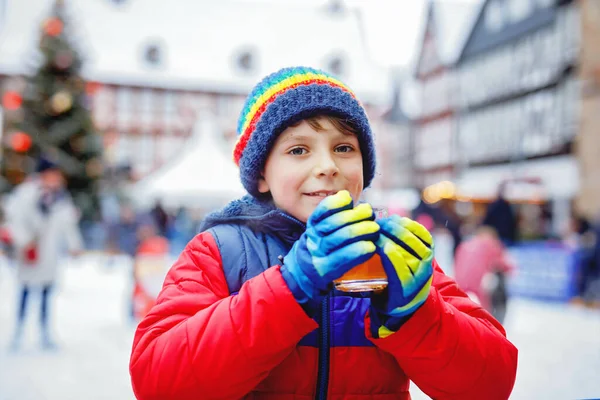 Happy little kid boy in colorful warm clothes on skating rink of Christmas market or fair drinking hot punch or chocolate. Healthy child having fun on ice skate. people having active winter leisure — Stock Photo, Image